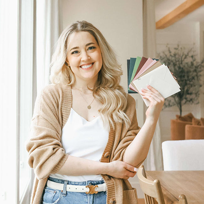 Alexis Austin, founder of Curio Press, smiling and holding colorful stationery paper samples in her St. Louis studio