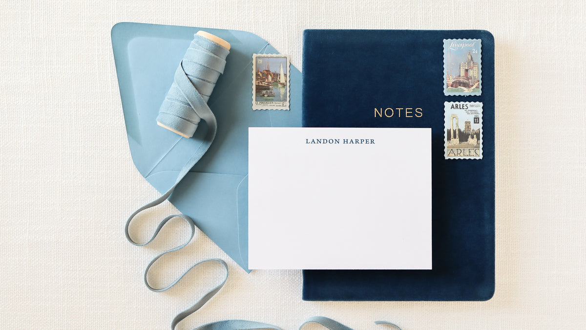 Personalized flat note card on navy leather journal with vintage postage stamps and linen ribbon